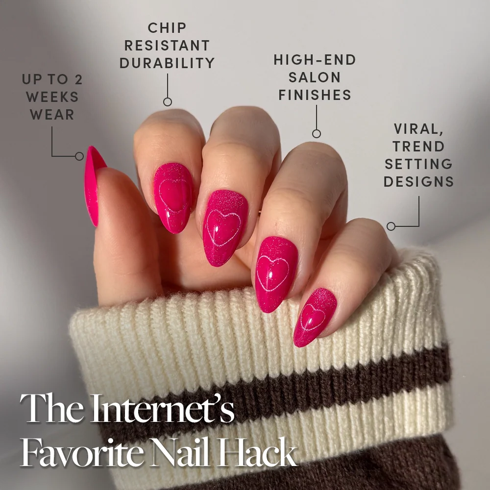 A hand with glossy, hot-pink velvet "Text Me Back" nails by glamnetic in heart patterns is shown. Features include up to 2 weeks’ wear, chip-resistant durability, salon-quality finish, and viral designs. Sweater sleeves are visible.