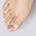 A close-up of a foot featuring Glamnetic press-on toenails in a shimmering shade of nude with a sparkle for an elegant look.