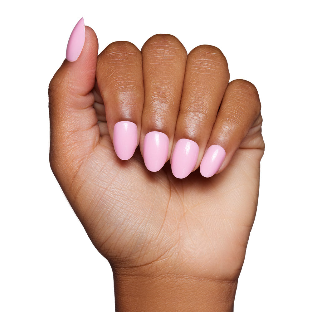 A hand with medium brown skin tone displays glamnetics Think Pink press-on nails, featuring neatly manicured, glossy baby pink polish, against a white background.