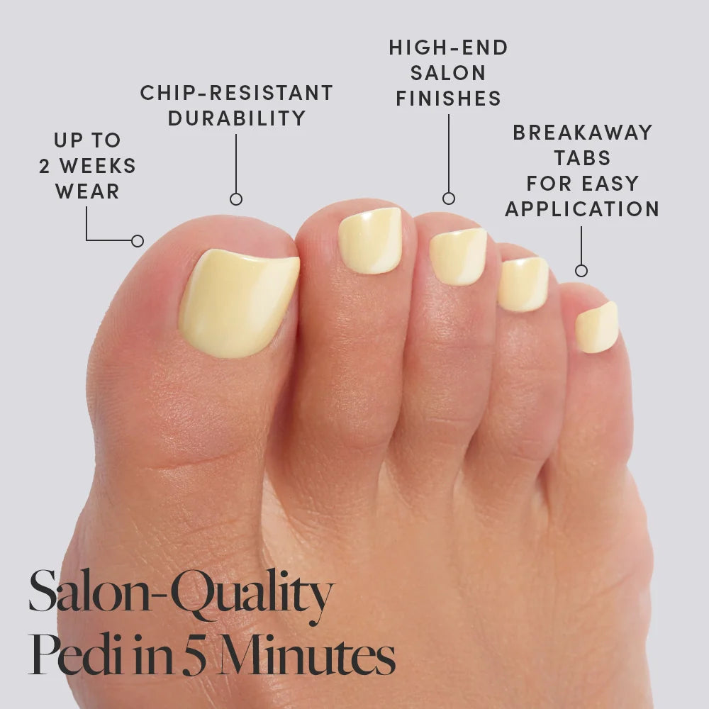 A foot wearing creamy pastel yellow shade Glamnetic press-on toenails with product features called out, including salon finish and 2-week wear.
