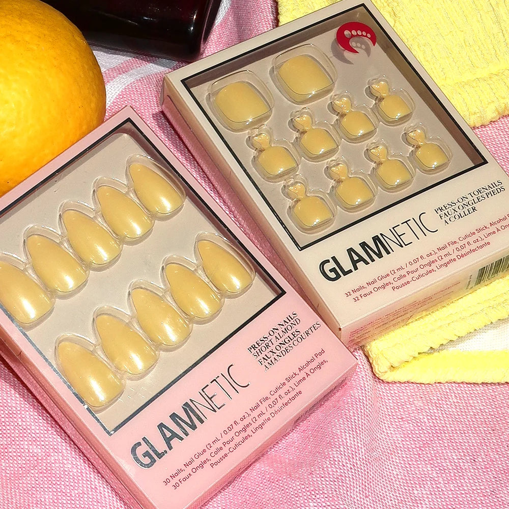 Glamnetic pastel yellow press-on nail sets in a box on a pink surface.