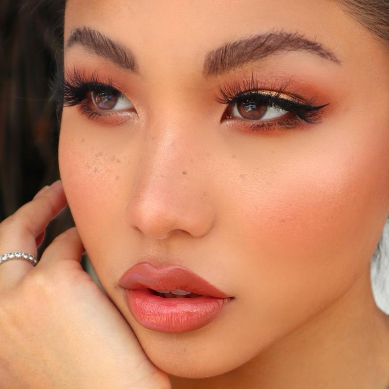 Close-up of a woman with smooth, glowing skin and winged eyeliner created with glamnetic Black Liquid Magnetic Liner (Reward), long lashes, defined brows, peachy blush, nude lipstick, and a silver ring on her finger.
